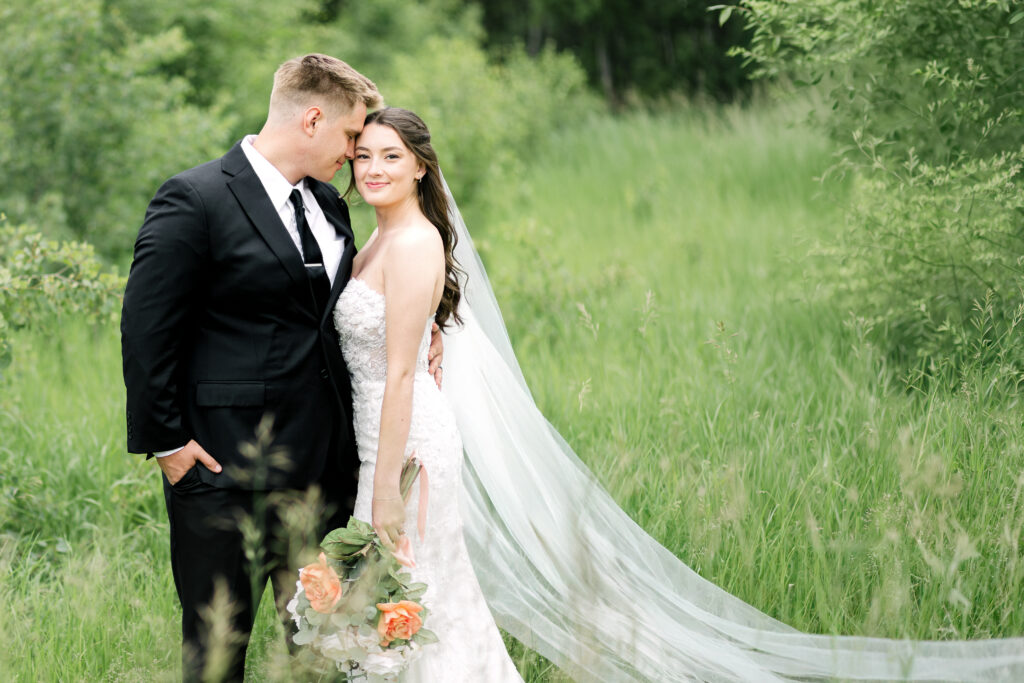 Fine art wedding couple in field with greenery, flowing veil and soft natural light in Winnipeg
