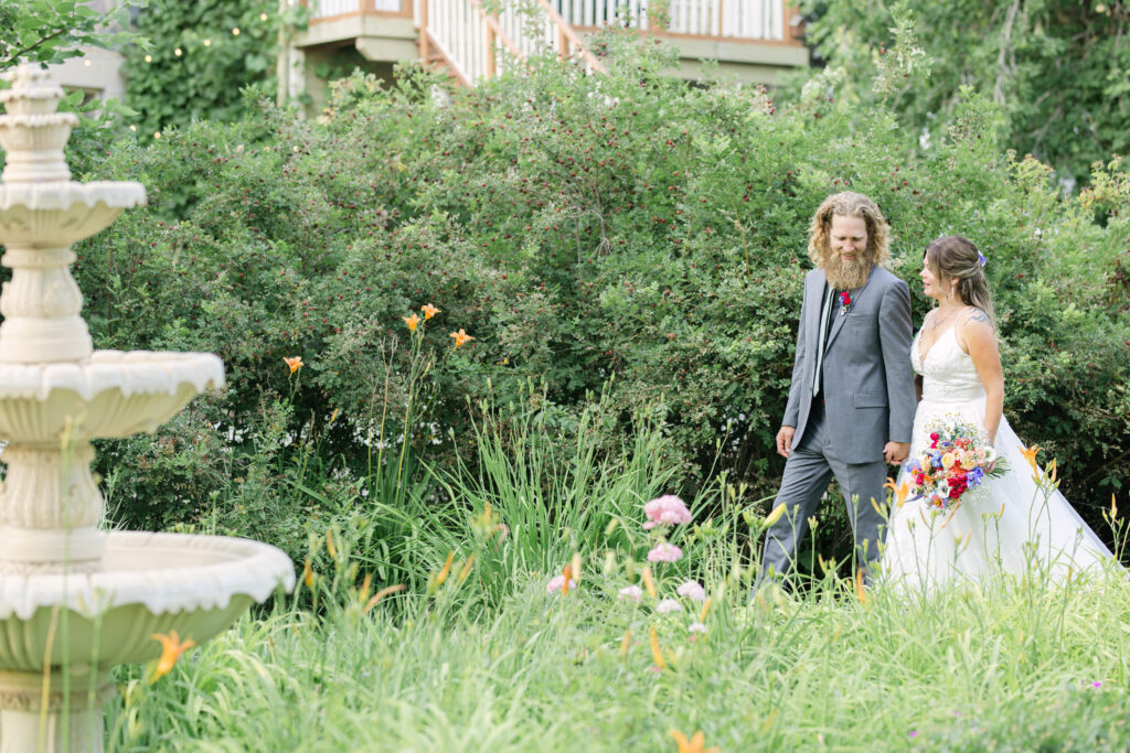 Couple walking through lush garden at Bella’s Castle in Morden Manitoba during engagement session with soft natural light