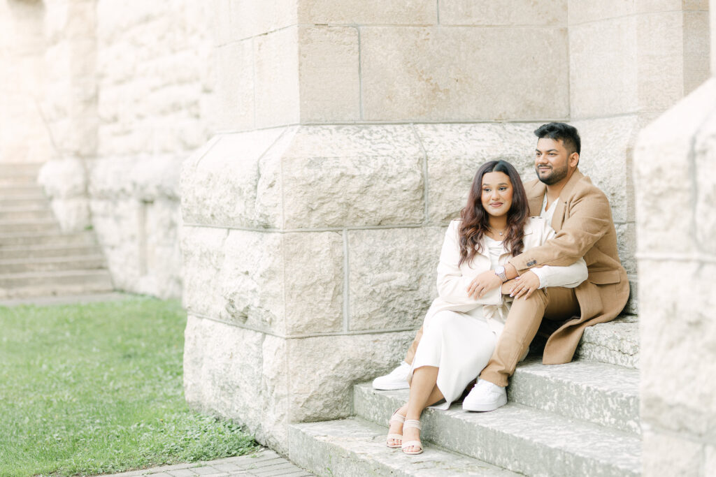 Couple sitting together on stone steps at St Boniface Cathedral Ruins in Winnipeg with soft natural light and romantic connection