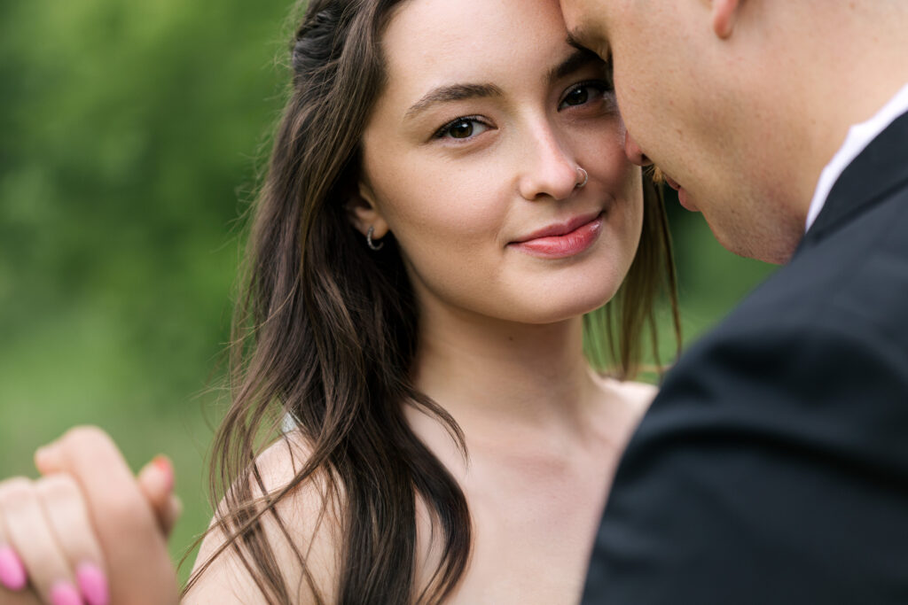 Close-up of bride looking at camera while groom leans in during wedding photos in Winnipeg Manitoba with soft natural light